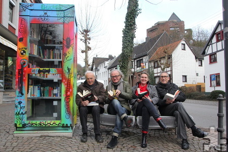 Frank Günter Zehnder (v.l.), Michael Koch, Brit Possardt und Peter Cremer nehmen auf der Bank neben dem Bücherschrank Platz und lesen. Foto: Thomas Schmitz/pp/Agentur ProfiPress